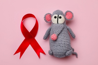 Cute knitted toy mouse and red ribbon on pink background, flat lay. AIDS disease awareness