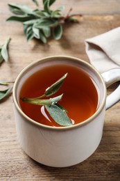 Cup of aromatic sage tea with fresh leaves on wooden table