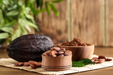 Bowls of cocoa beans and powder near pod on table
