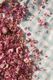 Photo of Scattered dried tea rose flowers and petals on checkered fabric, top view
