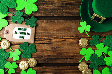 Frame made of clover leaves, gold coins and leprechaun hat on wooden table, flat lay with space for text. St. Patrick's Day celebration