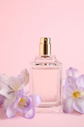 Bottle of perfume with freesia flowers on pink background