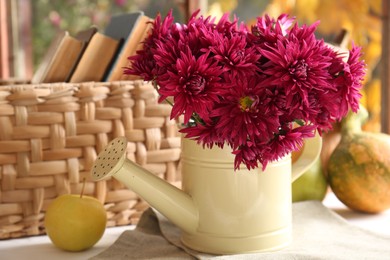 Photo of Beautiful chrysanthemum flowers in watering can and ripe apple on table indoors. Autumn still life