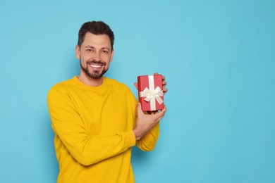 Photo of Happy man with gift box on light blue background, space for text