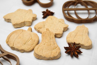 Photo of Baked biscuits of different shapes and cookie cutters on white table, closeup