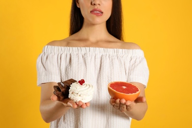 Concept of choice. Woman holding sweets and grapefruit on yellow background, closeup