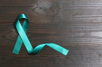 Teal awareness ribbon on wooden background, top view with space for text. Symbol of social and medical issues