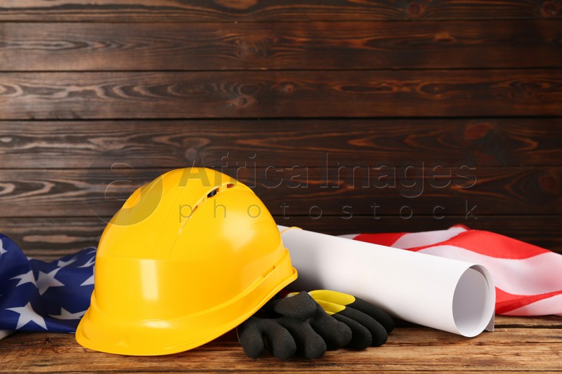 Yellow protective hard hat, gloves, construction drawing and American flag on wooden table