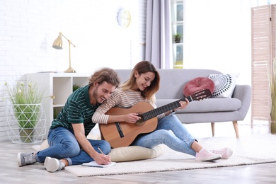 Young couple playing acoustic guitar and composing song in living room