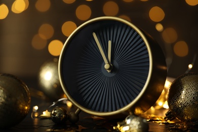 Stylish clock with decor on black table against blurred Christmas lights, closeup. New Year countdown