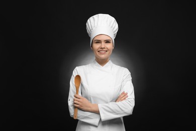 Photo of Happy female chef with wooden spoon on black background