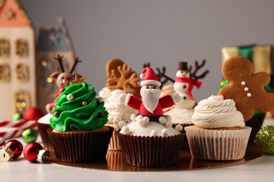 Different beautiful Christmas cupcakes and baubles on white table