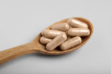 Gelatin capsules in spoon on light grey background, closeup
