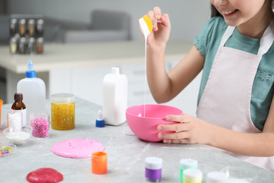 Little girl mixing ingredients with silicone spatula at table in kitchen, closeup. DIY slime toy