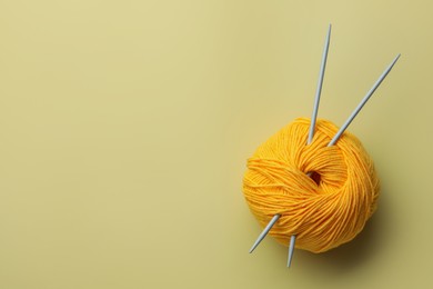 Photo of Soft woolen yarn and knitting needles on yellow background, top view. Space for text