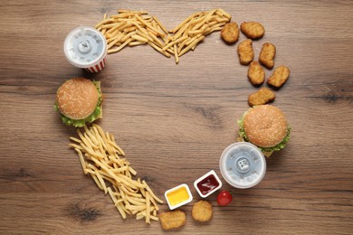 Photo of Heart shaped frame of delicious fast food menu on wooden table, flat lay. Space for text