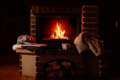 Knitwear and books near fireplace with burning wood indoors. Winter vacation
