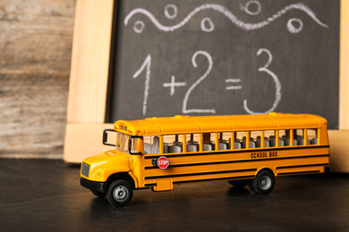 School bus model on black table near chalkboard. Transport for students