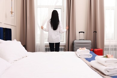Photo of Businesswoman opening window curtains in hotel room, back view