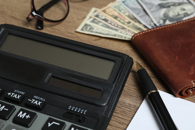 Calculator, pen and wallet with money on wooden table, closeup. Tax accounting
