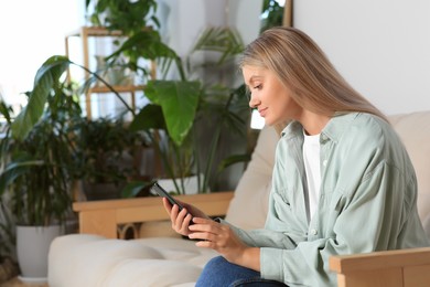 Photo of Woman using smartphone on sofa at home. Space for text