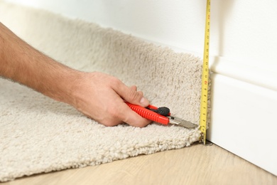 Worker with cutter knife and measuring tape installing new carpet indoors, closeup