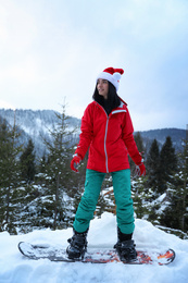 Young snowboarder wearing Santa hat on snowy hill. Winter vacation