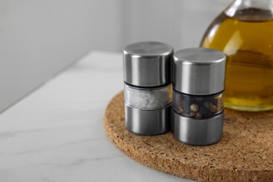 Salt and pepper mills with bottle of oil on white marble table, closeup. Space for text