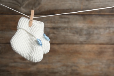 Pair of knitted booties on laundry line against wooden background, space for text. Baby accessories