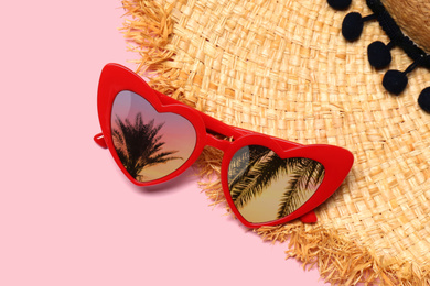 Heart shaped sunglasses with reflection of palm trees on pink background, flat lay 