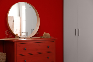 Round mirror and chest of drawers near red wall in room. Modern interior design