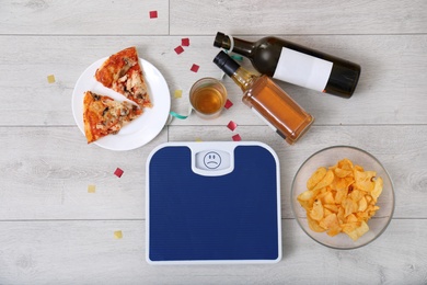 Digital scales, junk food and alcohol on wooden floor after party, top view
