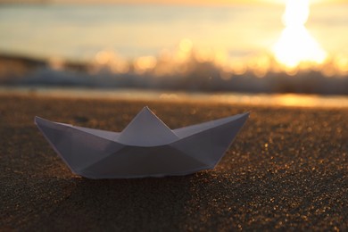 White paper boat on sand near sea at sunset, closeup. Space for text