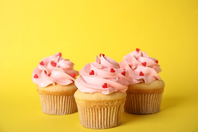 Tasty cupcakes with heart shaped sprinkles on yellow background. Valentine's Day celebration