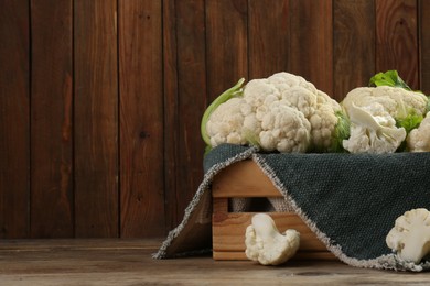 Photo of Crate with cut and whole cauliflowers on wooden table. Space for text