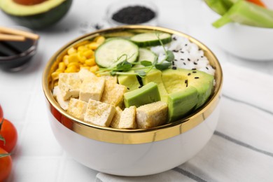 Photo of Delicious poke bowl with vegetables, tofu, avocado and microgreens on white tiled table, closeup