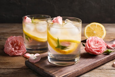 Delicious refreshing drink with lemon and roses on wooden table