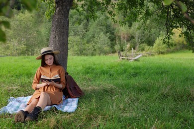 Young woman reading book under tree on meadow