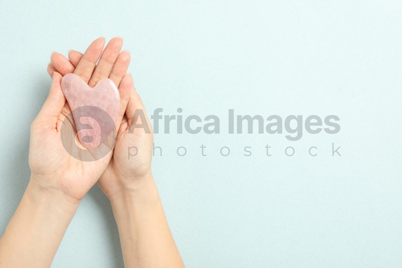 Photo of Woman with rose quartz gua sha tool on light blue background, closeup. Space for text