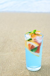 Glass of refreshing drink with grapefruit and mint on sandy beach