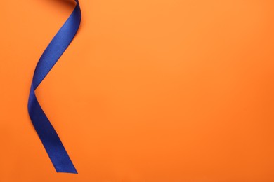 Photo of Beautiful blue ribbon on orange background, top view. Space for text