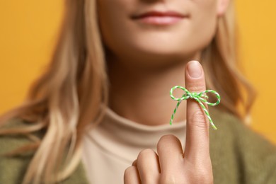 Photo of Woman showing index finger with tied bow as reminder against orange background, focus on hand