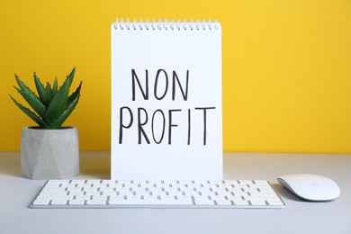 Notebook with phrase Non Profit, keyboard and houseplant on white table