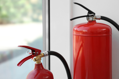 Different fire extinguishers near window indoors, closeup