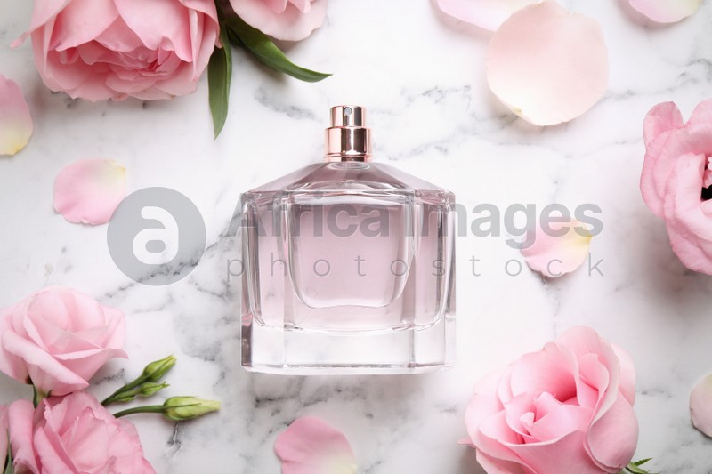 Bottle of perfume, beautiful flowers and petals on white marble table, flat lay