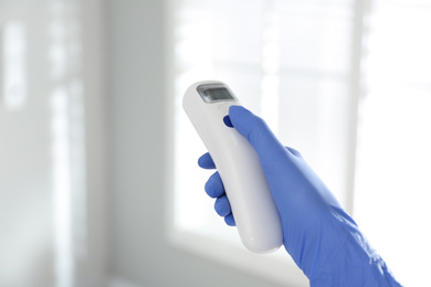 Doctor holding non contact infrared thermometer indoors, closeup. Measuring temperature