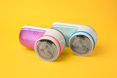Photo of Modern fabric shavers in different colors on yellow background, closeup