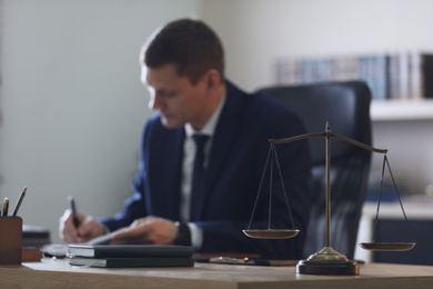 Male lawyer working at table in office, focus on scales of justice