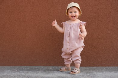 Cute little girl wearing stylish clothes near brown wall outdoors. Space for text
