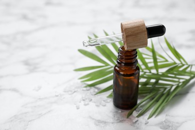 Bottle of essential oil and green twig on white marble table, closeup. Space for text